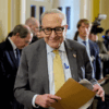 Senate Minority Leader Chuck Schumer walking through the halls of Congress smiling holding a folder.