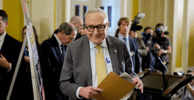 Senate Minority Leader Chuck Schumer walking through the halls of Congress smiling holding a folder.