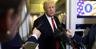 President Donald Trump speaks to members of the press on Oct. 19 aboard Air Force One. He is wearing a red tie and surrounded by microphones and journalists.