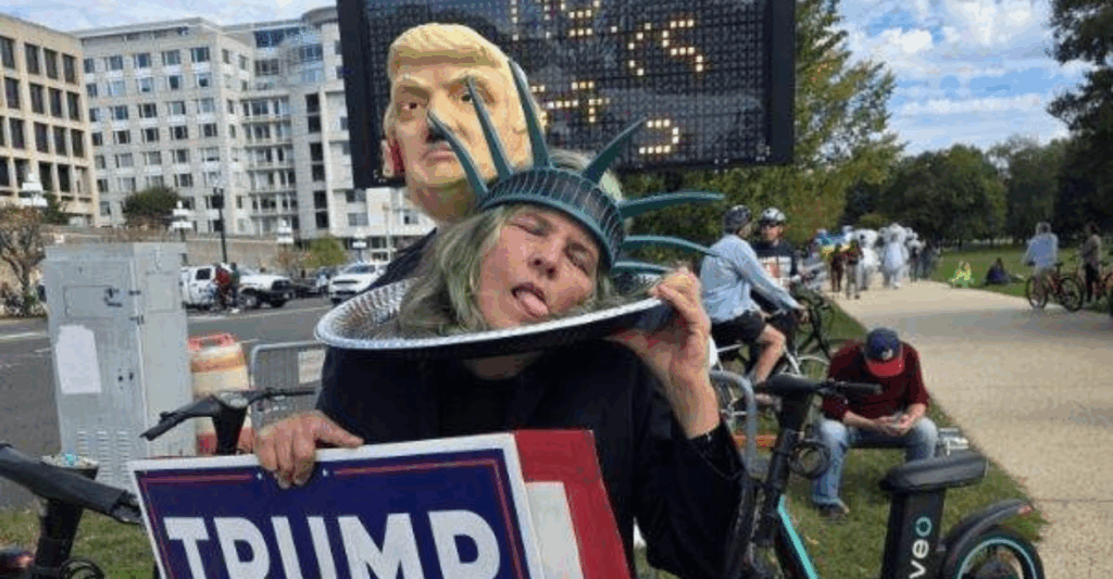 A woman dressed as the Statue of Liberty plays dead on a silver platter, with a mannequin of Trump surging from behind.