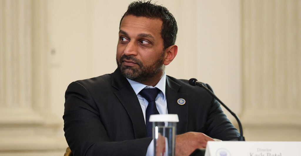 Kash Patel, seated, with a glass of water in front of him, looks to his right.