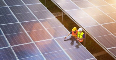 Aerial view of two solar energy technicians examining large solar panels in a field.