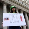 A young woman stands in front of a courthouse holding a sign reading "Free Luigi."