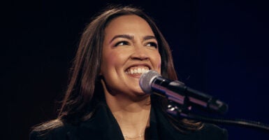 Alexandria Ocasio-Cortez smiles as she stands before a microphone.