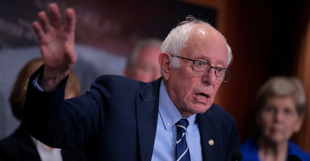 Bernie Sanders stands and gestures with his right hand in the air as he speaks.