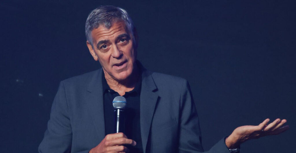 Actor George Clooney, with a microphone in his right hand and gesturing with his left hand