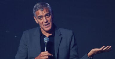 Actor George Clooney, with a microphone in his right hand and gesturing with his left hand