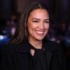 Alexandria Ocasio-Cortez stands at an event and smiles while she celebrates.
