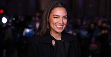 Alexandria Ocasio-Cortez stands at an event and smiles while she celebrates.