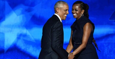 Michelle Obama and Barack Obama hold each other's hands as they stand together on a stage while smiling.