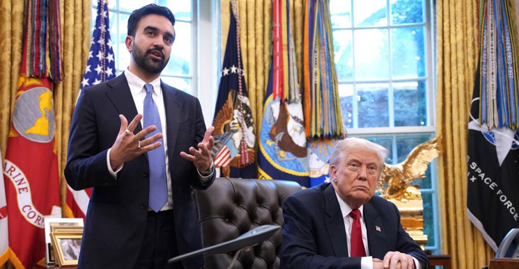 Zohran Mamdani stands in the White House and gestures with both his hands as he talks to reporters as Donald Trump looks on.