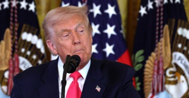 Donald Trump stands in front of a microphone and looks down and to his left.