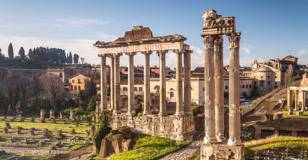 The ruins of the Temple of Saturday from ancient Rome stand on a sunny day.