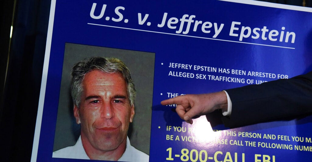 A hand points to a blown up photo of Jeffrey Epstein.