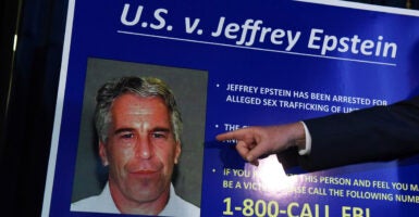 A hand points to a blown up photo of Jeffrey Epstein.