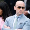 Stephen Miller, arms folded, in light blue suit stands next to wife Katie.