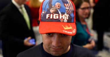 A young man wearing a hat with iconic Trump fist raised "Fight" photo looks dejected.