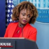 Karine Jean-Pierre at White House podium in red suit.