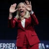 Abigail Spanberger, in red suit and white blouse, holds her hands in front of her face during her victory rally.