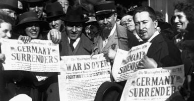 Historic photo of people holding up newspapers touting "Germany Surrenders," ending World War I.