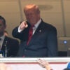 President Trump in the Commanders owner's box smiles and points at crowd.