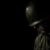 Somber, black-and-white profile of helmeted soldier, head bowed against a black background.