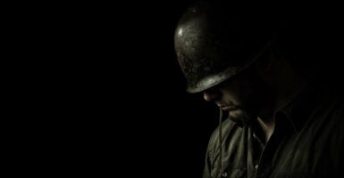 Somber, black-and-white profile of helmeted soldier, head bowed against a black background.