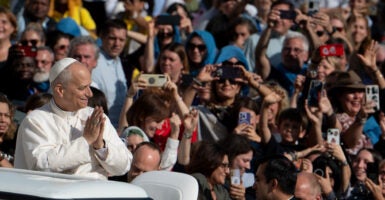 Pope Leo XIV holds hands together in prayer while Popemobile passes through crowd of students.