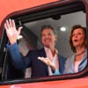 Gavin Newsom and Nancy Pelosi wave from a red electric train car.