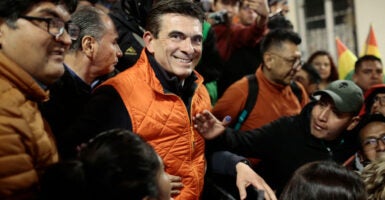 Rodrigo Paz in an orange down vest smiles as he is surrounded by supporters.