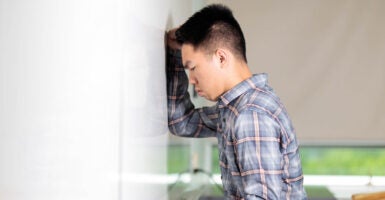 Asian student puts his head against classroom white board.