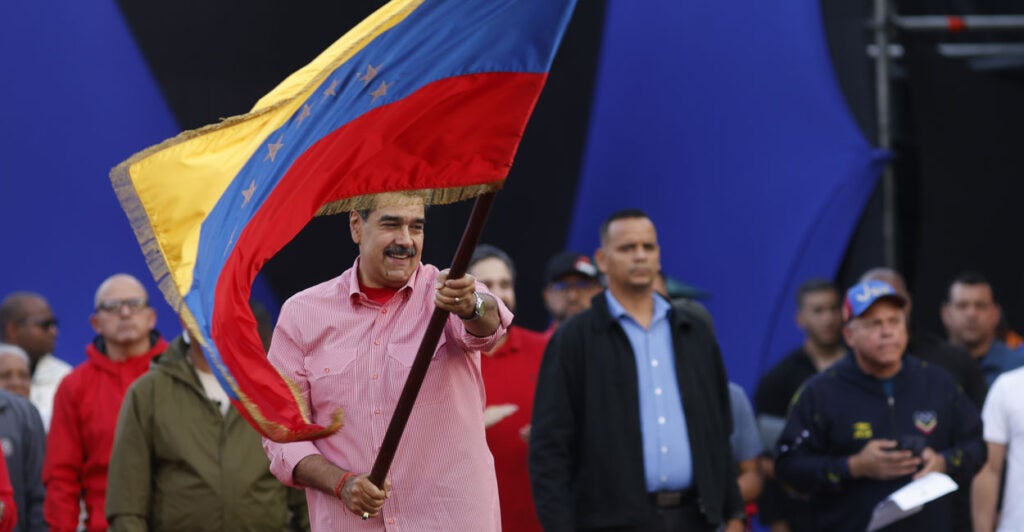 Venezuelan President Nicolas Maduro in a pink shirt waves Venezuelan flag.