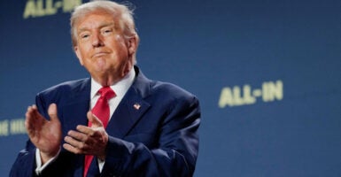 President Donald Trump clapping, against a blue backdrop reading 