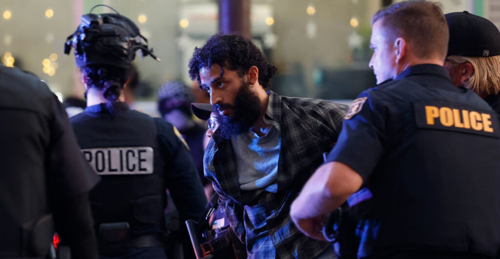 Bearded protester being led away in handcuffs by police.