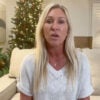 Majorie Taylor Greene in a white shirt, sitting on a couch with a Christmas tree behind her.