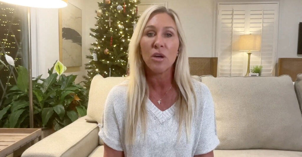 Majorie Taylor Greene in a white shirt, sitting on a couch with a Christmas tree behind her.