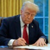 President Trump signing an executive order at his desk in the Oval Office.