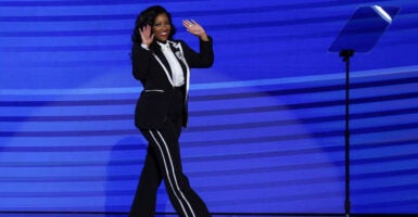 Jasmine Crockett, in a black suit with white shirt strolls across the stage with her hands raised.