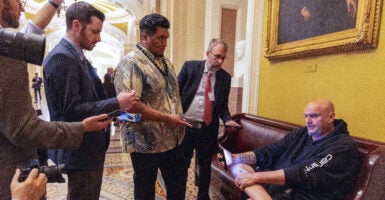U.S. Sen. John Fetterman (D-PA) sits on a couch speaking to reporters outside the Senate Chamber at the U.S. Capitol.