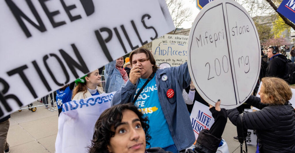 Demonstrators hold up signs outside U.S. Supreme Court, including one that says Mifepristone 200mg.