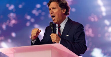 Tucker Carlson with fists clenched speaks at pink podium.