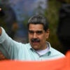 Nicolas Maduro gestures during a rally and holds his right hand up in the air.