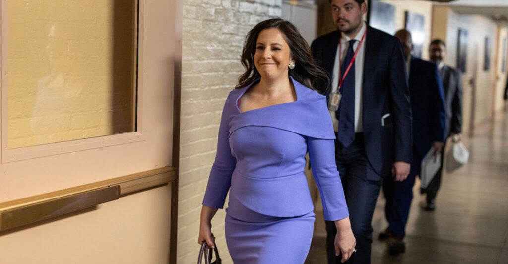 Elise Stefanik walks down a hallway as she carries a bag in her right hand.
