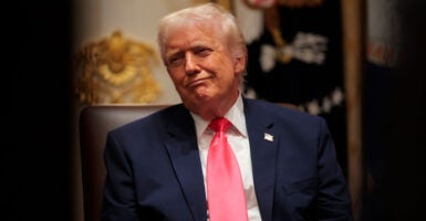 Donald Trump is seated and looking to his left as he makes a facial expression.