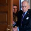 Chuck Grassley walks through a doorway while holding the door with both hands.