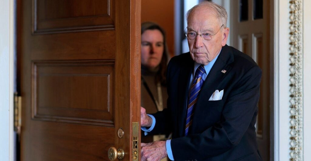 Chuck Grassley walks through a doorway while holding the door with both hands.
