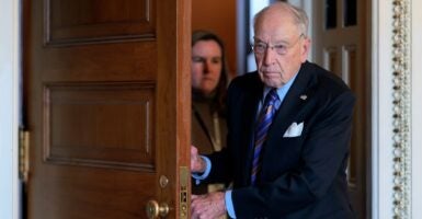 Chuck Grassley walks through a doorway while holding the door with both hands.