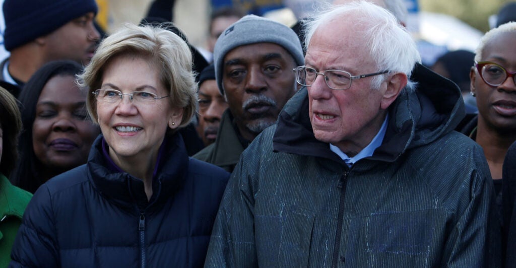 Sens. Elizabeth Warren and Bernie Sanders stand next to each other in winter coats during an outdoor rally.