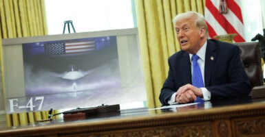 Donald Trump sits at his Oval Office desk next to an artist rendering of the F-47 fighter currently being developed.