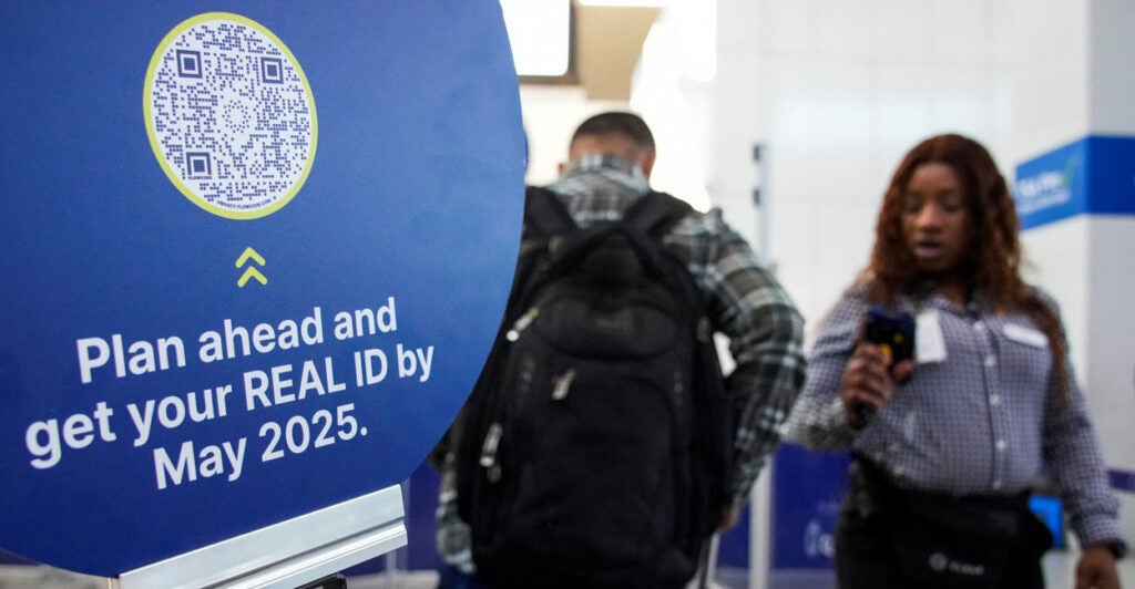 TSA agent checks out a passenger next to a sign advertising Real ID.